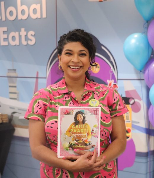 Chef Aarti Sequeira posing in the Appleton North commons with her cookbook Aarti Paarti: An American Kitchen with an Indian Soul